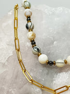 Détail du Collier Rivage en perles de coquillage sur un fond rocheux, montrant la texture des perles et les petites perles dorées intercalaires.