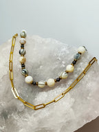 Collier Rivage en perles de coquillage, élégamment posé sur une roche claire, mettant en valeur sa simplicité et ses finitions dorées.