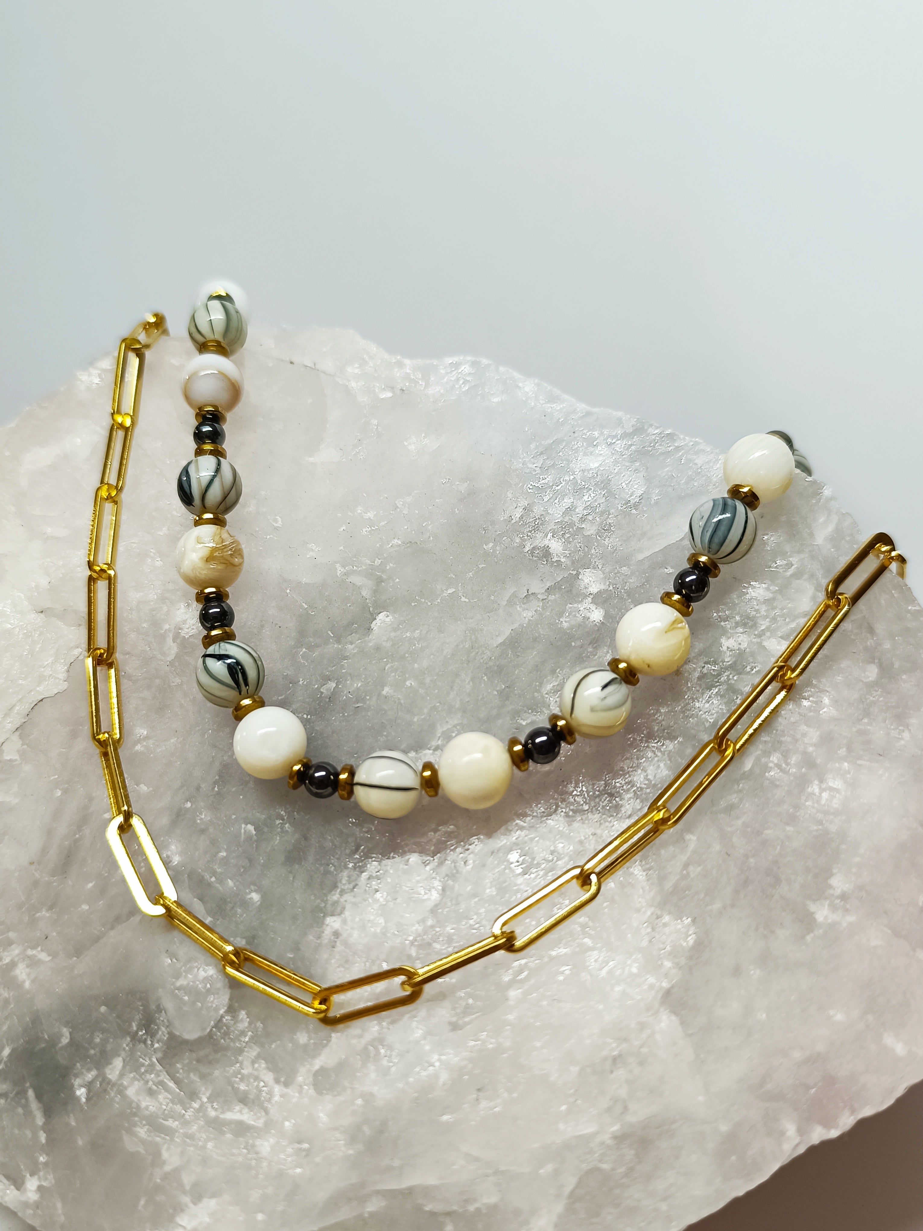 Collier Rivage en perles de coquillage, élégamment posé sur une roche claire, mettant en valeur sa simplicité et ses finitions dorées.
