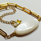 Gros plan du Bracelet AVA en nacre naturelle ovale blanche et chaîne dorée, avec un pendentif étoile et une petite perle blanche.