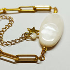 Détail du Bracelet AVA montrant la perle de nacre naturelle ovale irisée et la chaîne maillons dorée sur fond blanc.