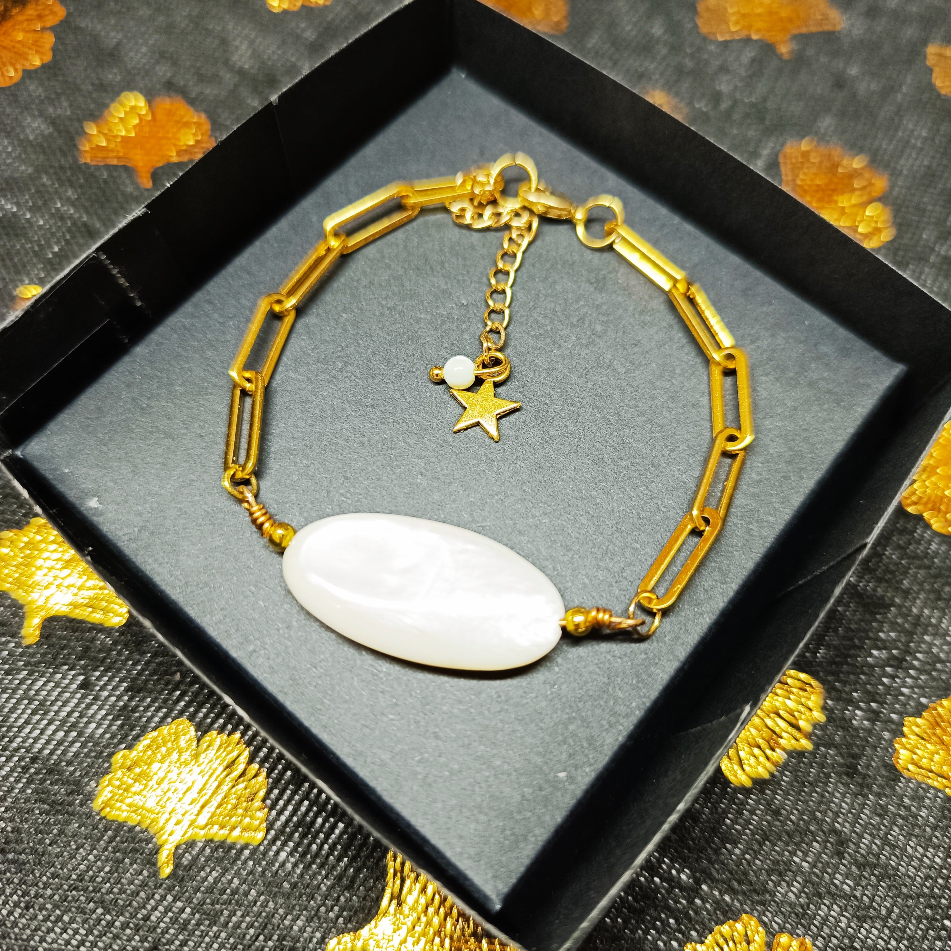 Bracelet AVA en nacre naturelle et chaîne dorée, avec pendentif étoile, présenté dans un élégant écrin noir.