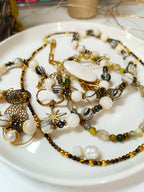 Assortiment de bijoux artisanaux dorés : colliers en perles de coquillage Rivage, bracelets Agate Mousse avec pendentif libellule, et autres créations en pierres naturelles et acier inoxydable.

