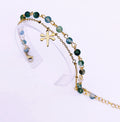 Bracelet double SANACA en Agate Mousse et acier inoxydable doré avec pendentif libellule, présenté sur un support transparent.
