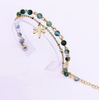 Bracelet double SANACA en Agate Mousse et acier inoxydable doré avec pendentif libellule, présenté sur un support transparent.