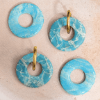 Présentation à plat de quatre pampilles rondes Agate en pâte polymère marbrée bleu ciel et blanc, dont deux montées sur de simples anneaux dorés lisses.