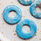 Zoom sur les détails et les finitions brillantes de deux pampilles rondes Agate bleues à marbrures blanches et inclusions de feuilles d'or scintillantes.