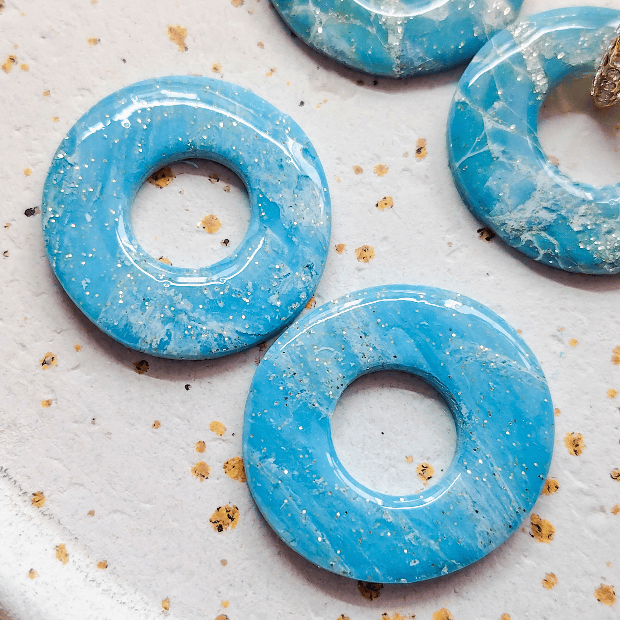 Zoom sur les détails et les finitions brillantes de deux pampilles rondes Agate bleues à marbrures blanches et inclusions de feuilles d'or scintillantes.