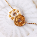 ccumulation de deux pendentifs totems artisanaux de la marque Sanaca sur une chaîne dorée : l'un en argile blanc nacré avec des étoiles dorées gravées, l'autre en finition entièrement texturée dorée effet émaillé.