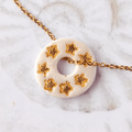 Gros plan sur le bijou artisanal fait main Totem Les Âmes, une pampille ronde de couleur blanche nacrée avec des motifs étoiles à la feuille d'or, glissée sur sa chaîne dorée à l'or fin.