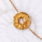 Gros plan sur le pendentif Le Soleil SANACA, texture artisanale dorée à la feuille d'or et reflets de mica sur marbre blanc.