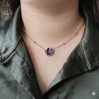 Pendentif artisanal "L'Enfant Intérieur" révélant son motif abstrait aux nuances violettes et turquoises, porté sur une fine chaîne dorée en acier inoxydable.