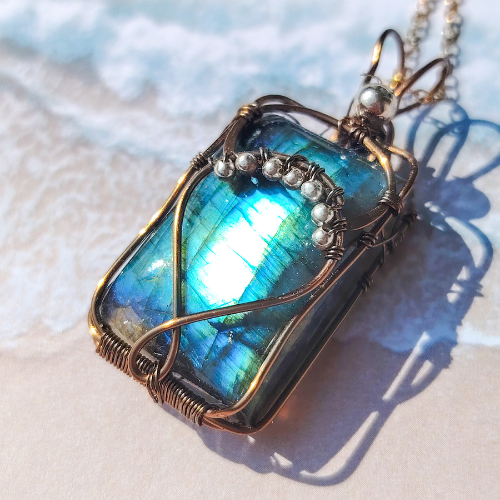 Gros plan du pendentif "Aura" en labradorite bleue irisée, orné de fil de laiton et perles argent 925, fait main en wire wrapping.
