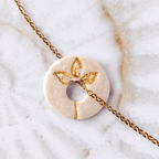 Détail du symbole Fleur gravé et doré à l'or sur médaille en céramique blanche artisanale.