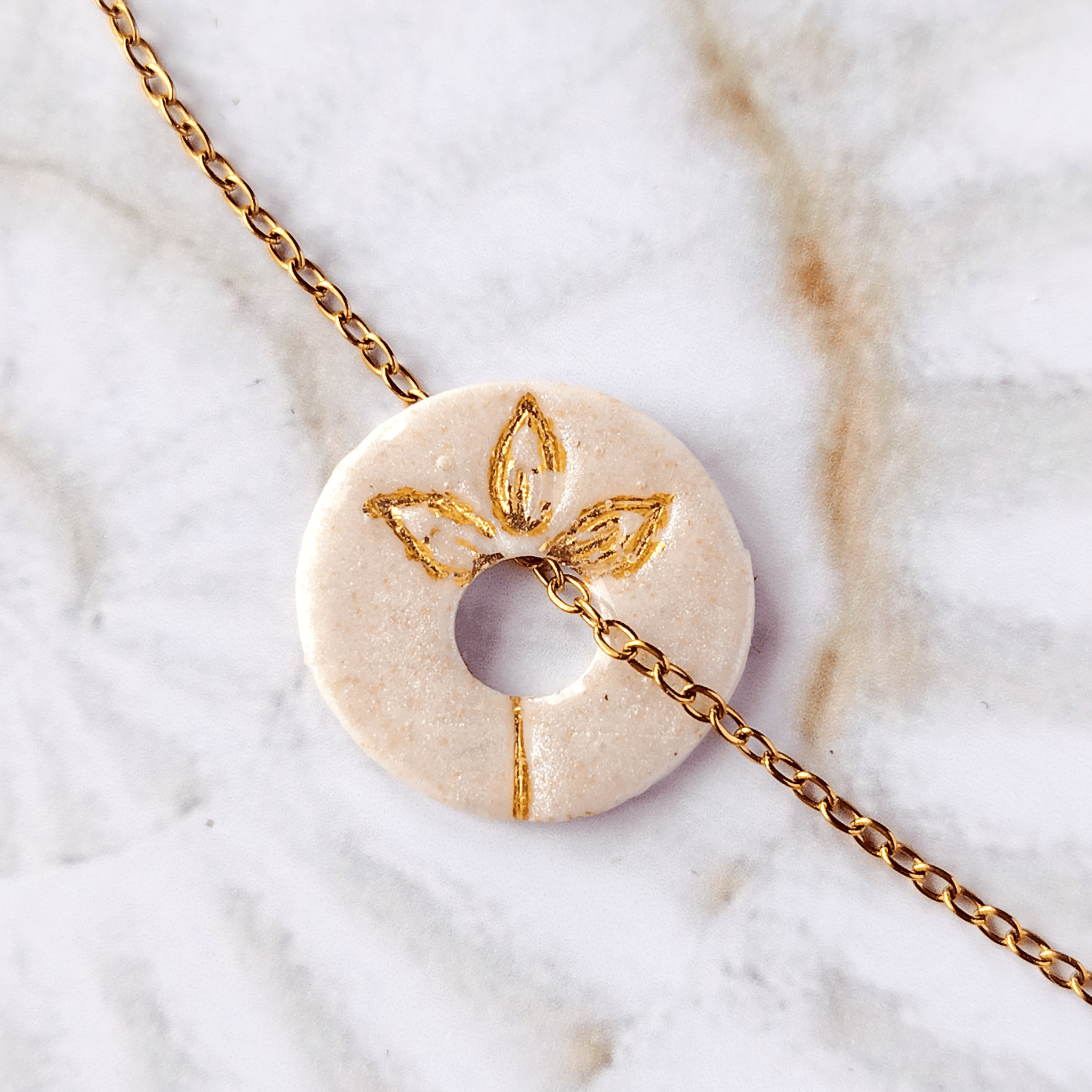 Détail du symbole Fleur gravé et doré à l'or sur médaille en céramique blanche artisanale.
