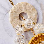 Zoom sur le Totem Spirale Le Murmure, une pièce unique avec perles de quartz transparent et pampille artisanale aux reflets dorés, Sanaca.