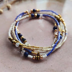 Un bracelet multi-tours pour femme enroulé, composé de perles naturelles de Lapis-Lazuli, de perles Miyuki blanches et d'hématite dorée, posé sur une surface texturée rose poudré.
