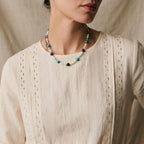 Collier Biarritz Sanaca porté au cou, mélange de pierres naturelles bleues et violettes avec perles d'eau douce sur une blouse en lin blanc.