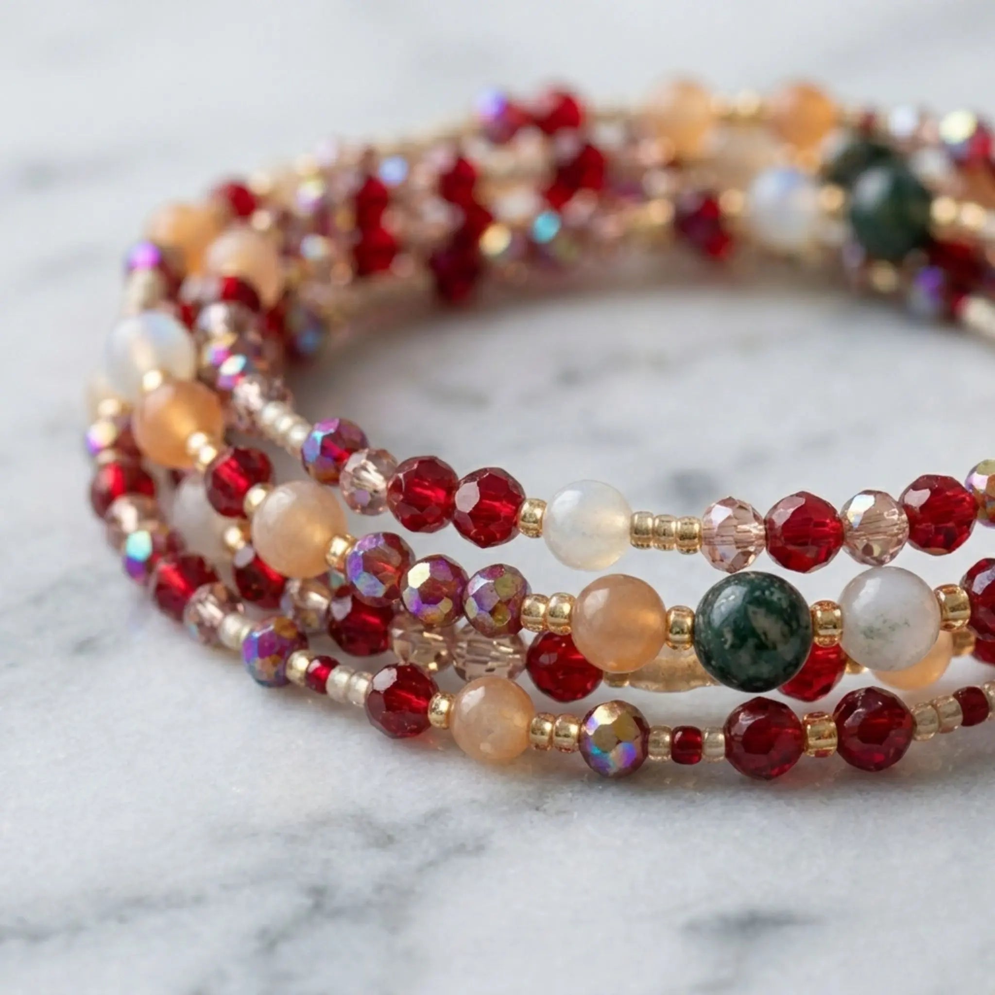 Un gros plan d'un collier bracelet minitours composé de perles rouges, orange et blanches, avec des accents dorés. Les perles de différentes tailles et couleurs sont enfilées sur plusieurs rangs, créant un motif complexe. Le collier est présenté sur un fond de marbre blanc