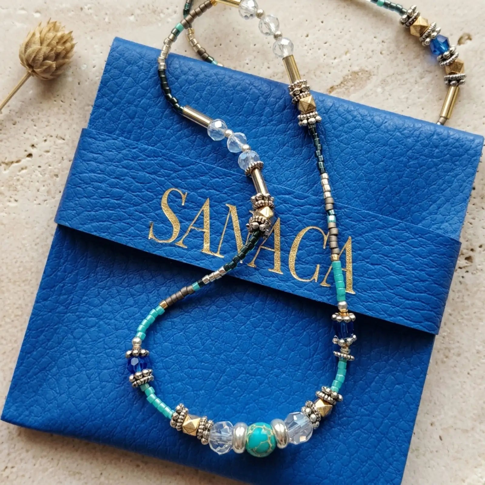 Collier 2-en-1 Sanaca en jaspe bleu présenté sur sa pochette signature en cuir bleu et marquage or.