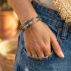 Une femme avec la main dans la poche de son jean en denim bleu porte le bracelet Luz au poignet. Le bracelet, avec ses perles turquoises, bleues et dorées, est enroulé plusieurs fois. On voit également d'autres bagues en or à ses doigts