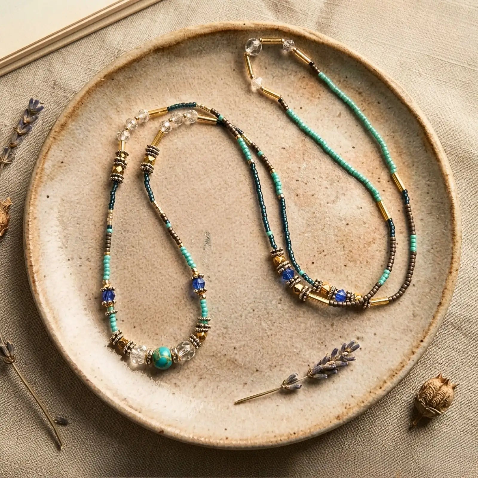 Collier 2-en-1 Luz exposé sur une assiette en céramique artisanale avec brins de lavande, photographie éditoriale de bijou en pierres naturelles turquoise et or.