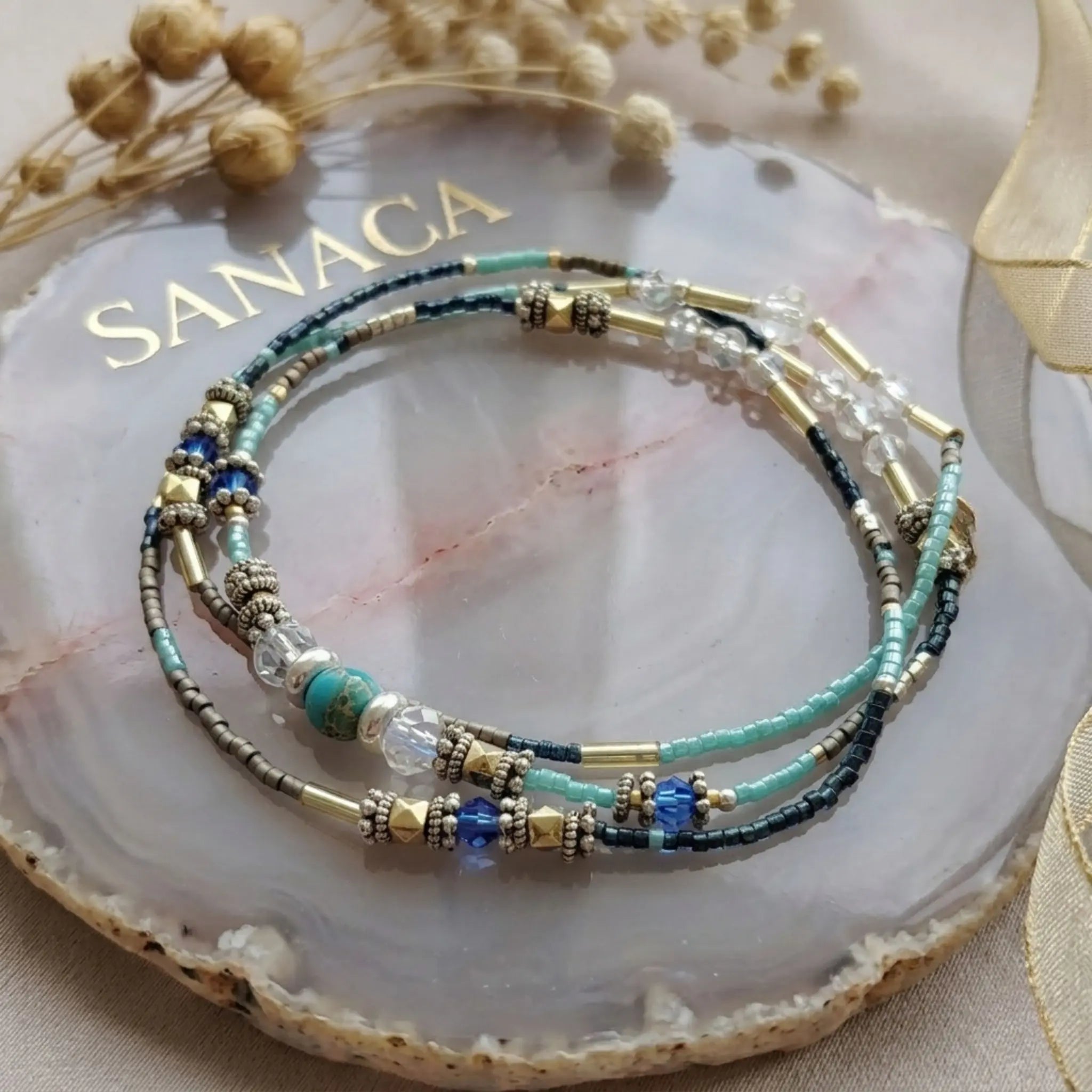 Bracelet 4 tours artisanal en jaspe et perles de verre Sanaca, présenté sur un support minéral avec logo doré.