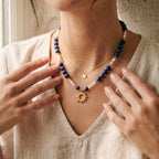 Portrait rapproché d'une femme portant le collier Solis en accumulation avec une fine chaîne dorée. Le contraste entre le bleu intense du lapis-lazuli, le blanc des perles d'eau douce et le lin de la blouse crée un look solaire et élégant typique du style artisanal du sud-ouest.