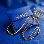 Packaging signature Sanaca Bijoux, pochette en cuir bleu électrique avec logo doré et collier Ambre, prêt à offrir.