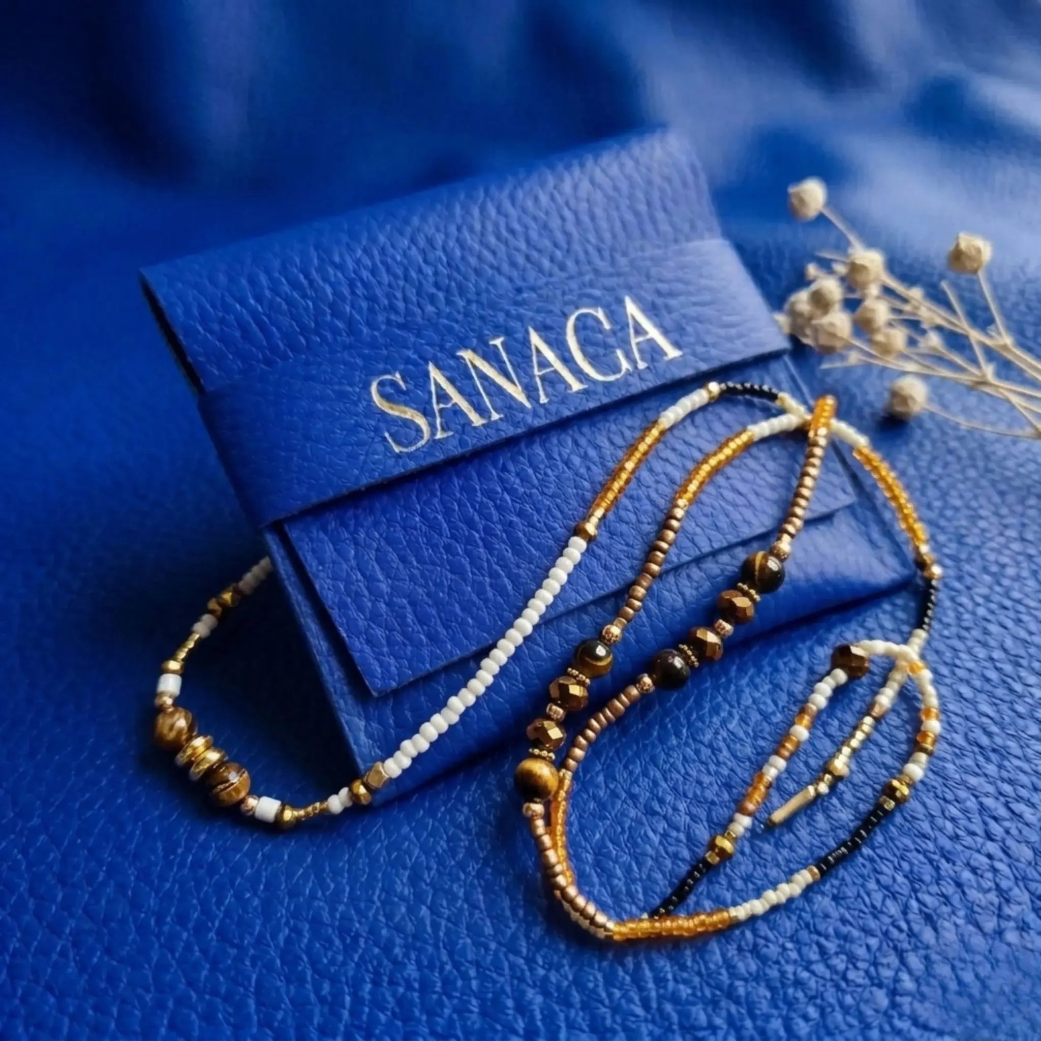 Packaging signature Sanaca Bijoux, pochette en cuir bleu électrique avec logo doré et collier Ambre, prêt à offrir.